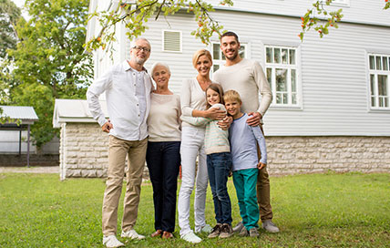 Family smiling and posing together in front of their house, creating a warm and inviting atmosphere with a sense of togetherness and happiness.